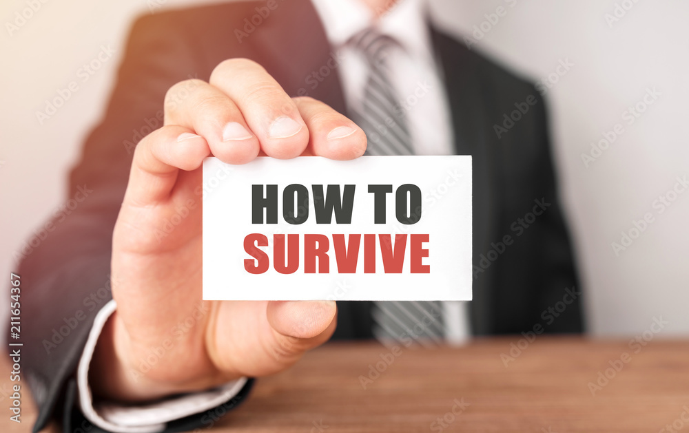 Businessman holding a card with text How to survive Businessman holding a card with text How to survive