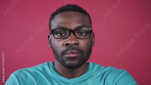 Nice brown-eyed African guy with beard putting black glasses, looking directly at camera. Young man in mint sweater. Close-up.