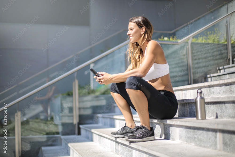 Woman wearing sportive clothes, sitting down on a stairs taking a break Woman wearing sportive clothes, sitting down on a stairs taking a break