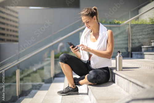 Sportive girl taking a break, sitting down on stairs and checking her phone