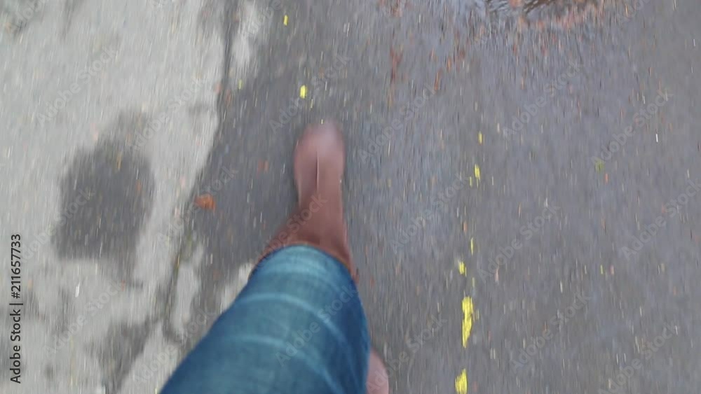 Point of view shot of female legs isolated on grey wet from rain pavement covered with golden fall leaves. Adult woman in brown leather boots walks outdoors in autumn nasty rainy day.