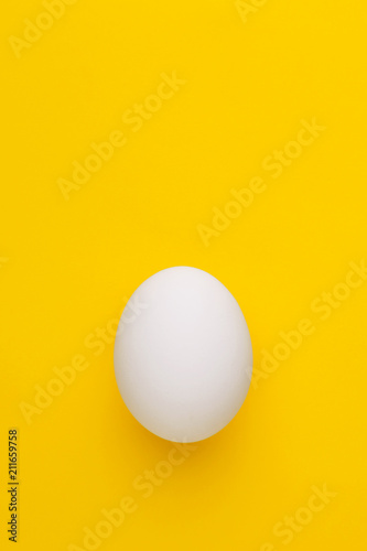 Single white chicken egg on a yellow background. Top view. Copy space