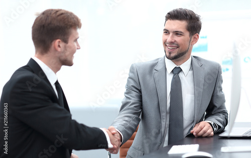 handshake of business partners sitting at a Desk.