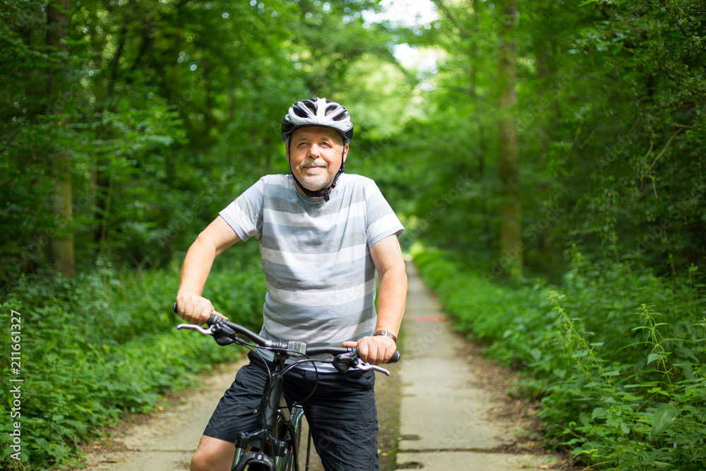 Obraz premium Senior man on a bike during lovely summer time in forest, smiling, enjoying trip