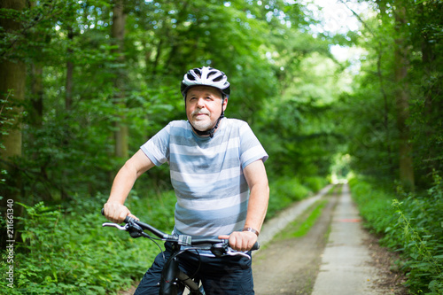 Senior man on a bike during lovely summer time in forest, smiling, enjoying trip © Khaligo