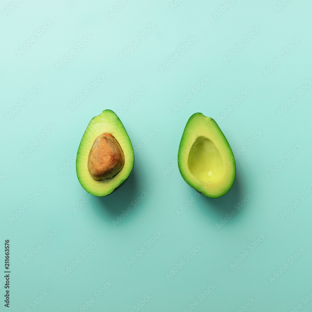 Green avocado halves with seed on blue pastel background. Creative minimal flat lay style with copy space. Summer food concept. Top view. Pop art design. Square crop. Green avocado halves with seed on blue pastel background. Creative minimal flat lay style with copy space. Summer food concept. Top view. Pop art design. Square crop.