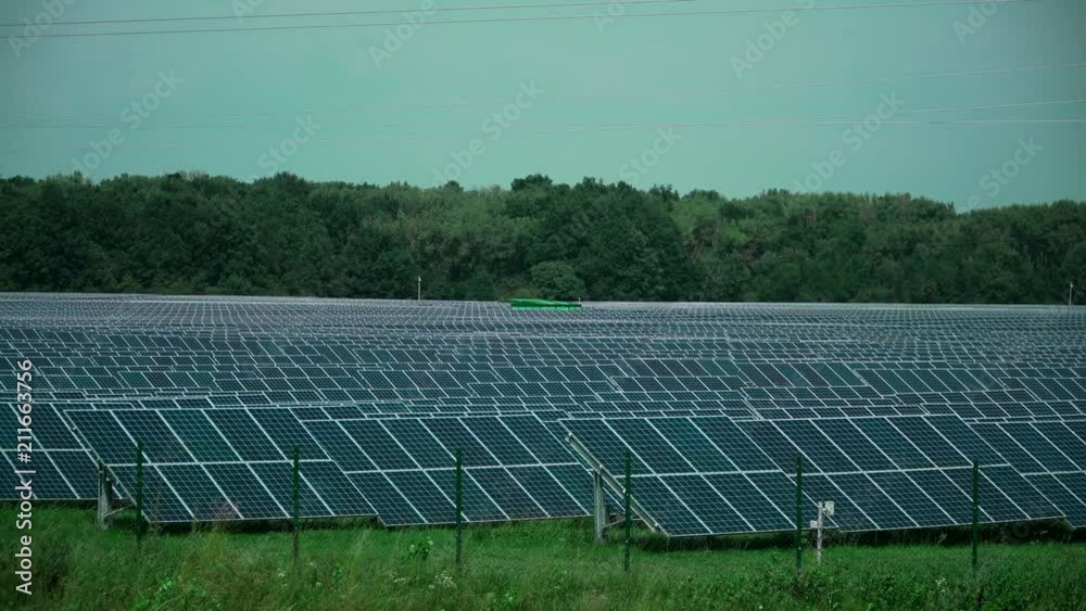 A rural landscape with solar power plants. The solar panels are arranged in rows, there are elec- tronic columns between them, against the background there is a green booth and forest A rural landscape with solar power plants. The solar panels are arranged in rows, there are elec- tronic columns between them, against the background there is a green booth and forest