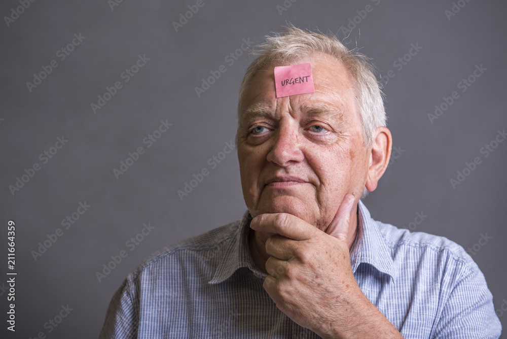 Mature man with an urgent note on his forehead, taken on a grey background Mature man with an urgent note on his forehead, taken on a grey background