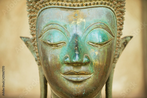 Close up of a face of an ancient copper Buddha statue outside of the Hor Phra Keo temple (former temple of the Emerald Buddha) in Vientiane, Laos.
