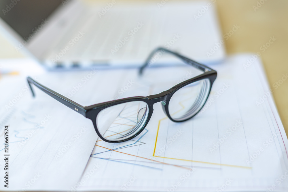 desk workplace, eyeglasses and laptop on report graph on wood  desk, business concept
