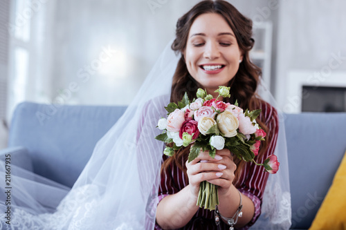 Wedding bouquet. Charming bride smiling broadly while holding nice wedding bouquet in her hands