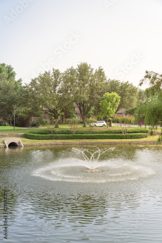Typical community lake with fountain spray in Coppell, Texas, America. Well-groomed tree landscaping and outfall sewer