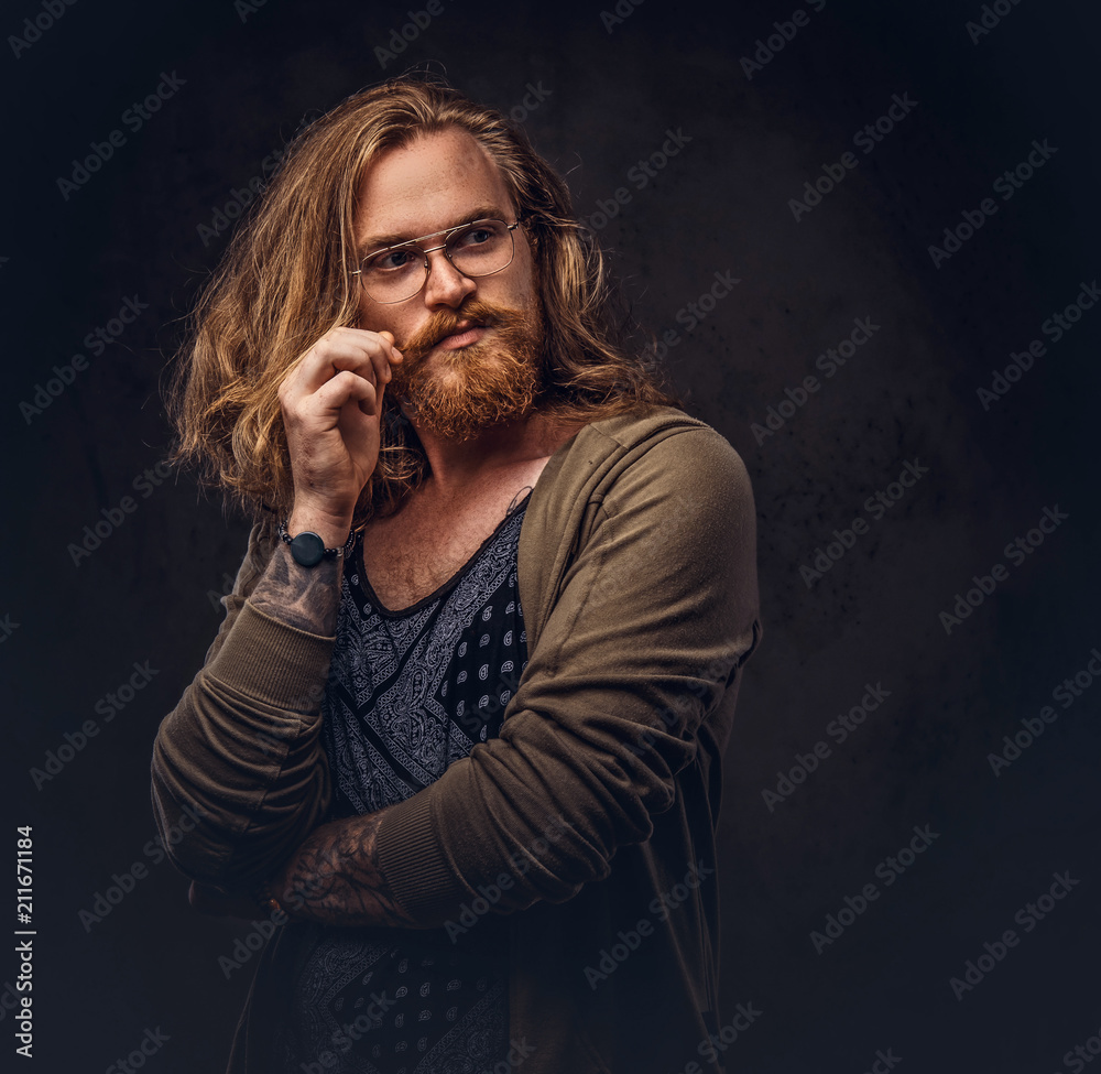 Portrait of tattoed redhead hipster male with long luxuriant hair and full beard dressed in a t-shirt and jacket holds a keeps the scarecrow of an owl and fox skin on a shoulder in a studio. Portrait of tattoed redhead hipster male with long luxuriant hair and full beard dressed in a t-shirt and jacket holds a keeps the scarecrow of an owl and fox skin on a shoulder in a studio.