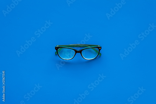One glasses with transparent lenses on blue background top view copy space