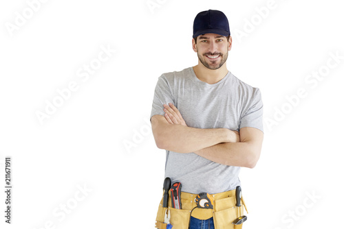 Portrait of young handyman standing at isolated white background with copy space. Successful repairman wearing baseball cap and tool belt. photo