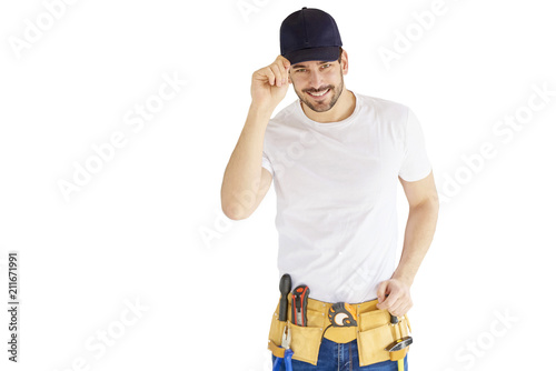 Portrait of young handyman standing at isolated white background with copy space. Successful repairman wearing baseball cap and tool belt. photo