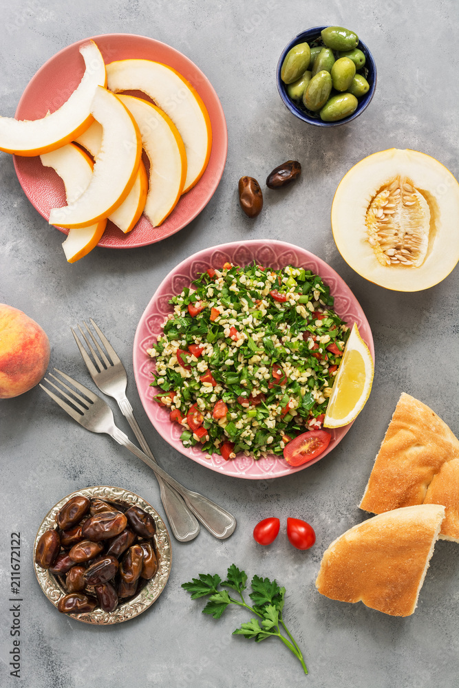 Lebanese traditional dish, the salad of parsley and bulgur tabbouleh on a gray concrete background. Different Eastern or Arabic food , melon,peach,dates,olives. flat lay Lebanese traditional dish, the salad of parsley and bulgur tabbouleh on a gray concrete background. Different Eastern or Arabic food , melon,peach,dates,olives. flat lay