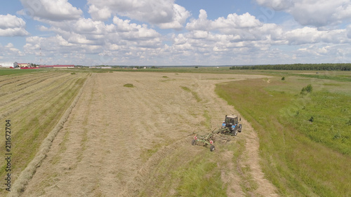 Aerial, view agricultural machinery with wheeled rake makes ranks beveled hay.Tractor which is lining up dried grass getting it ready for pickup so it can be used as animal fodder summer day.