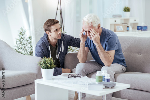 Stay strong. Upset senior man massaging temples while man looking at him