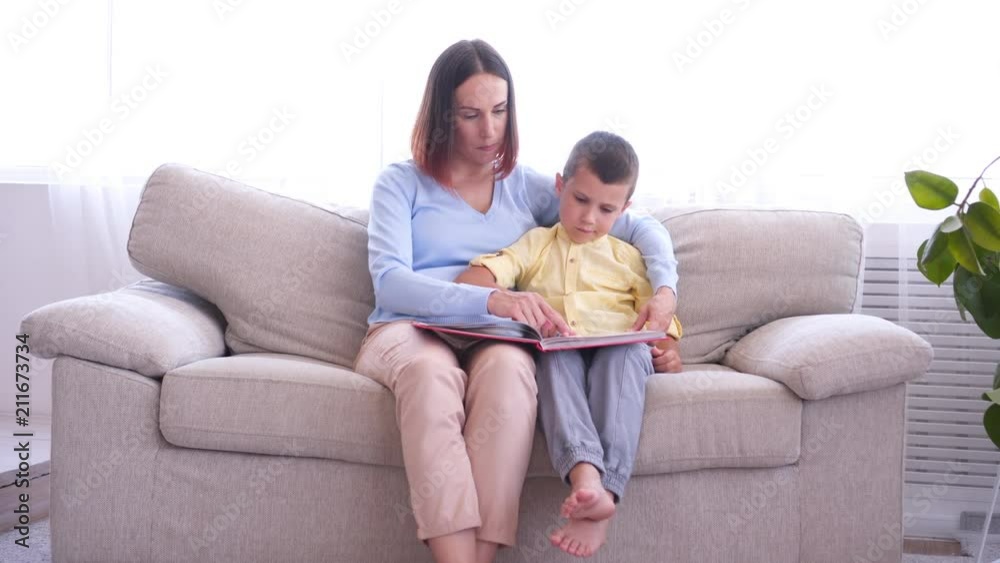 Mother and her son reading book while sitting in armchair on sunny day Mother and her son reading book while sitting in armchair on sunny day