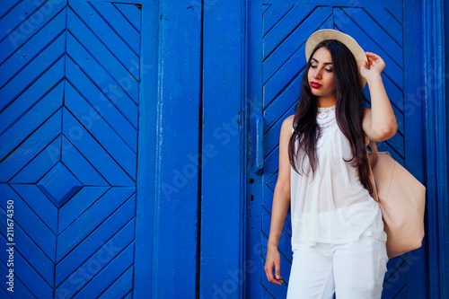 Happy tourist woman smiling against blue wooden door. Outdoor portrait of beautiful college girl wearing summer outfit