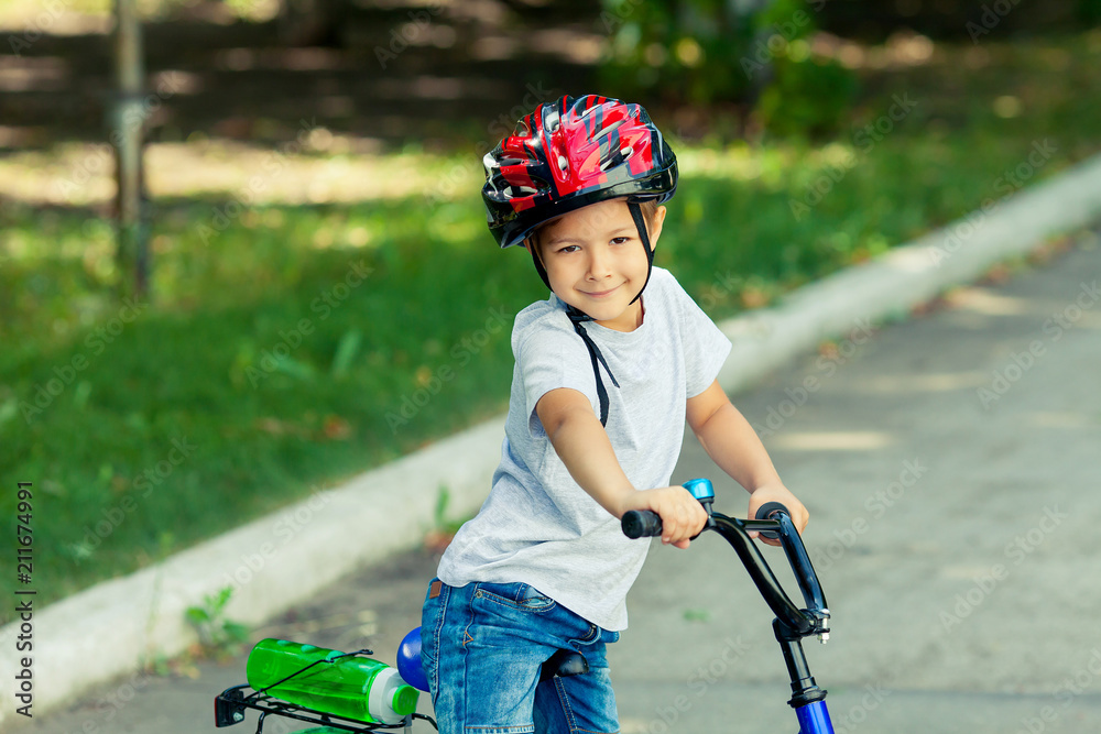 Obraz premium Little boy learns to ride a bike in the park near the home. Portrait of a cute kid on bicycle. Happy smiling child in helmet riding a cycling.
