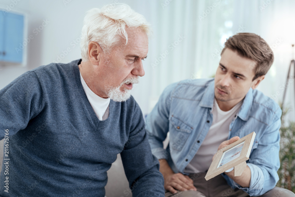 My family. Upset senior man talking and man holding photo