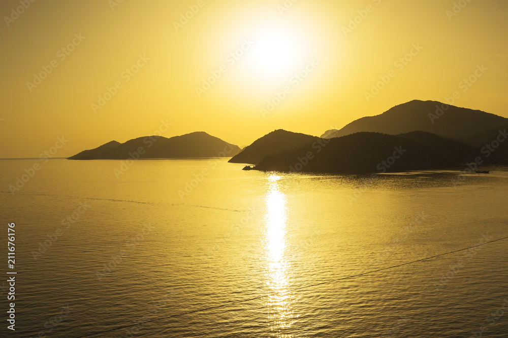 Mediterranean landscape. Sunset on the sea with flowing bright colored rays of the sun through the clouds.  Silhouettes of mountains. Background.