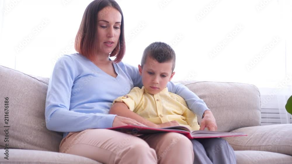 Mother sitting on couch and reading book with son Mother sitting on couch and reading book with son