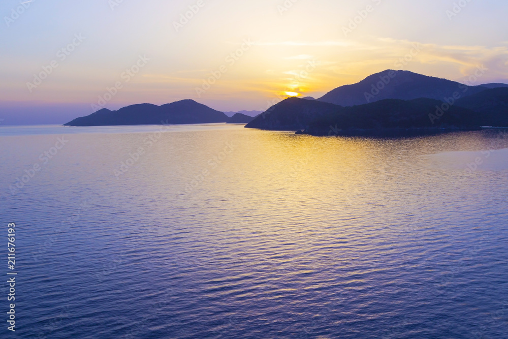 Mediterranean landscape. Sunset on the sea with flowing bright colored rays of the sun through the clouds. Silhouettes of mountains. Background. Mediterranean landscape. Sunset on the sea with flowing bright colored rays of the sun through the clouds. Silhouettes of mountains. Background.