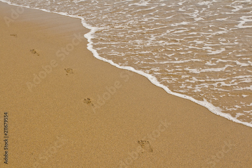 Footprints on the Sand Next to a Small Foamy Wave on the Beach