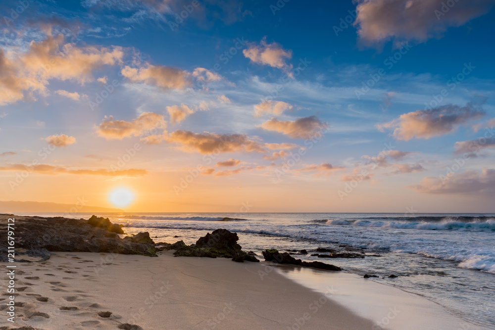 Sunset over Sunset Beach on the North Shore of Oahu, Hawaii with surf rolling in over coral rocks on the sandy beach