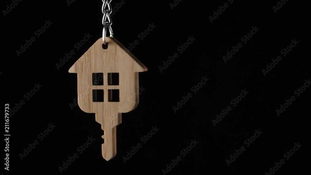 Wooden key holder with house shape hanging and rotating on black background