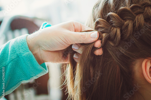 The hairdresser plaits the braid girl. Hands, close-up. Pretty haircut. photo