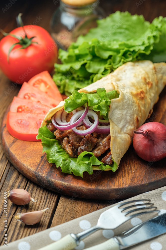 Doner kebab is lying on the cutting board. Shawarma with meat, onions, salad lies on a dark old wooden table.