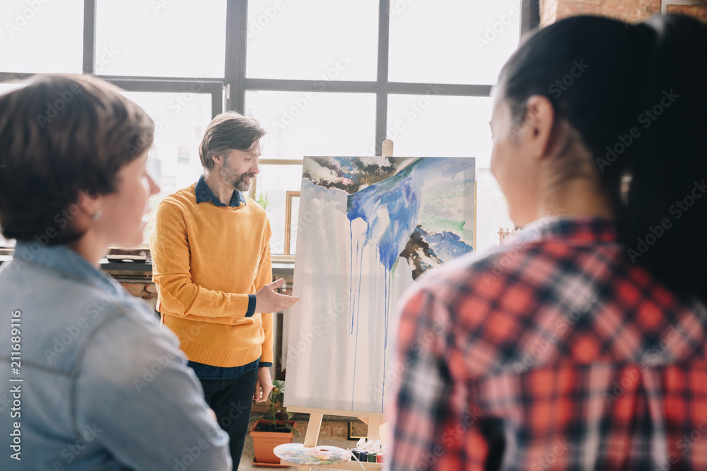 Fototapeta premium Portrait of mature bearded artist presenting watercolor painting to audience in art studio