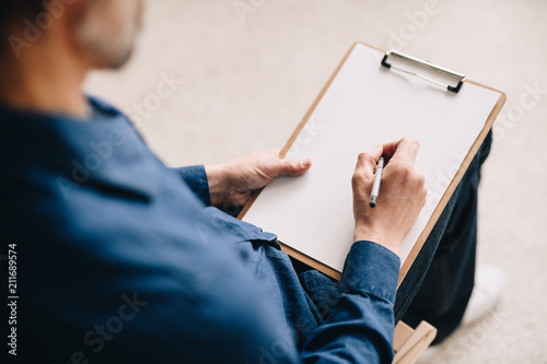Warm toned closeup  of unrecognizable mature man holding blank sheet of paper ready to write or sketch pictures, copy space