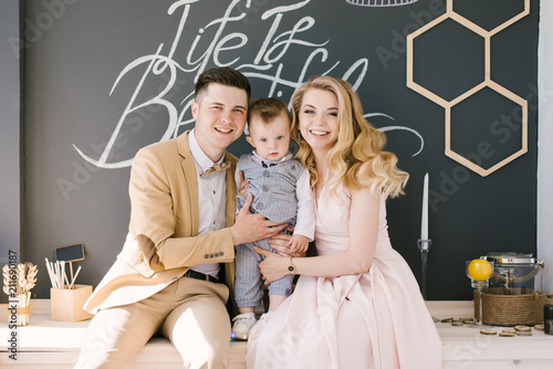 Beautiful young parents smile with their one-year-old child at home in a beautiful interior in pastel colors. Family look. Happy birthday party