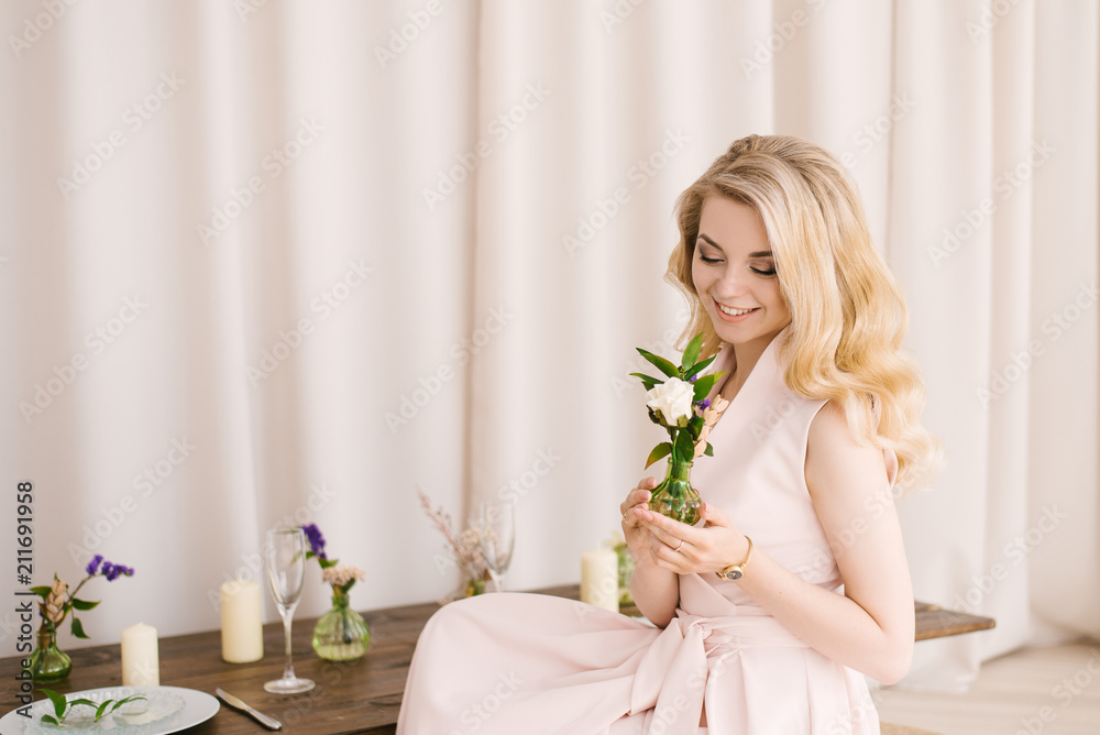 Portrait of a beautiful young girl with curly blonde hair in a delicate dress on a light background. Eyes look down with beautiful makeup closeup Portrait of a beautiful young girl with curly blonde hair in a delicate dress on a light background. Eyes look down with beautiful makeup closeup