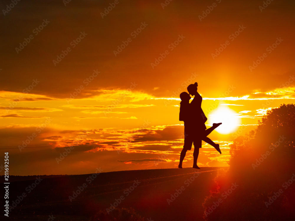Romantic couple on countryside at the sunset with the sun and one tree