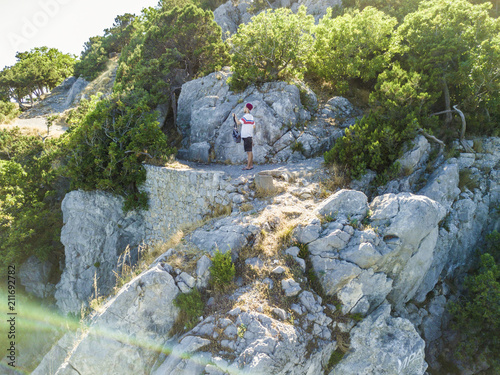 man in casual shirt and shorts with bag standing on the mountain edge and hiking to the top photo