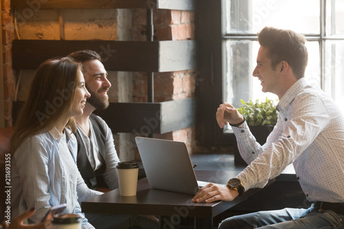 Male architect talking to smiling millennial couple, consulting on housing project, realtor explaining mortgage and contract condition to excited young couple during friendly meeting in coffee shop photo