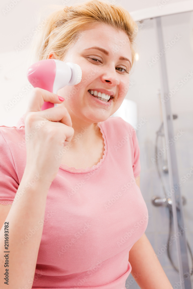 Happy woman using facial cleansing brush