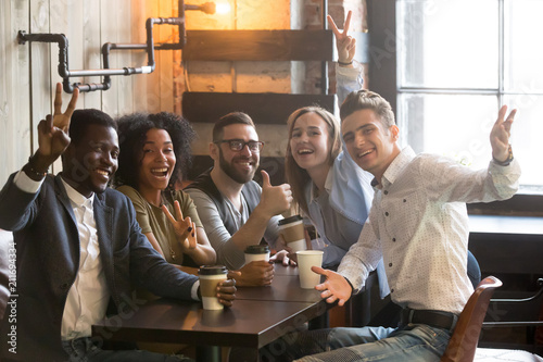 Portrait of smiling multiracial friends having fun together, drinking coffee in cafe, happy millennials posing to camera enjoying meeting in cafe, excited colleagues looking at camera chilling out