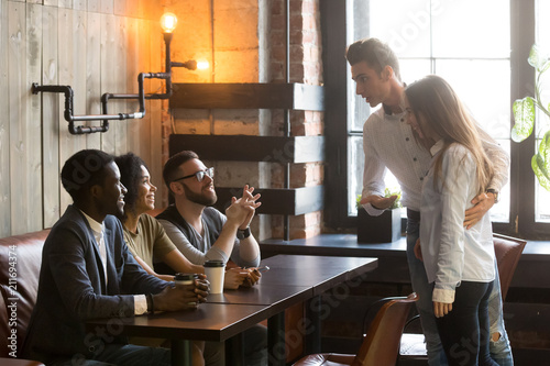 Caucasian man introducing girlfriend to multiracial millennial friends sitting at table, enjoying coffee in cafe, male worker acquainting colleagues with new female employee at meeting in coffeeshop photo