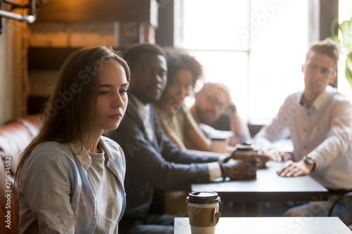 Konstfotografi Sad offended sitting alone in coffeeshop, ignoring people cheering her because of canceled date, female outcast not talking or listening to friends apologizing after bad joke