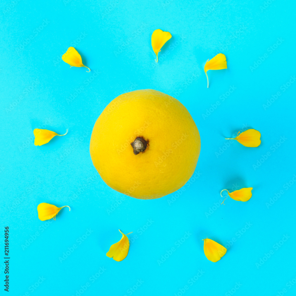 Yellow whole lemon in the form of the sun and rays from the petals of a yellow flower on a pastel blue background.