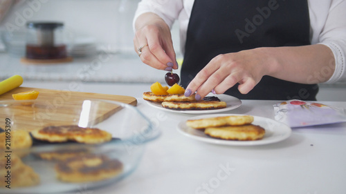 Woman is decorating with cherry cottage cheese pancakes in the kitchen © KONSTANTIN SHISHKIN