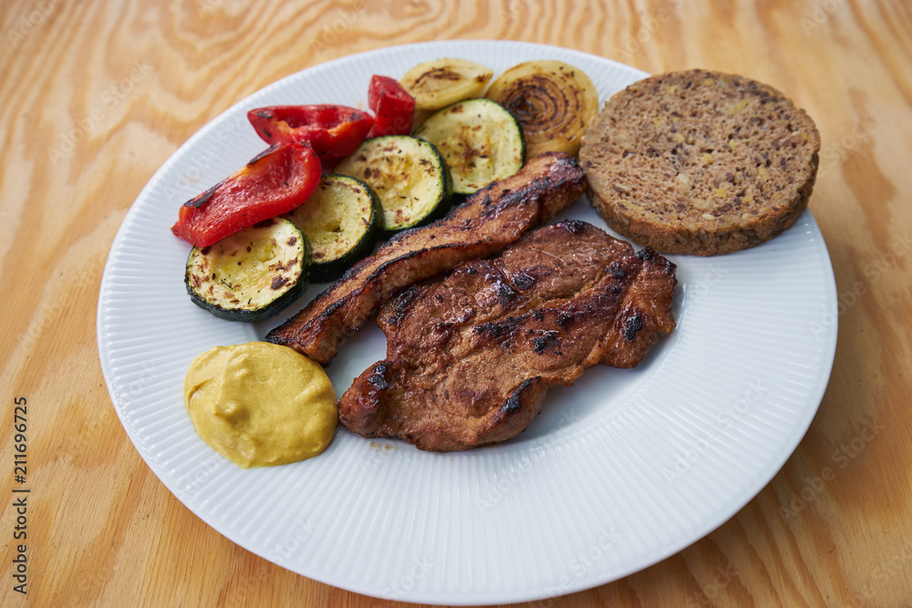 Detail of grilled pork meat consist from pork collar and streaky bacon served with grilled vegetables, zucchini, onion, red pepper and whole grain bread and  mustard.