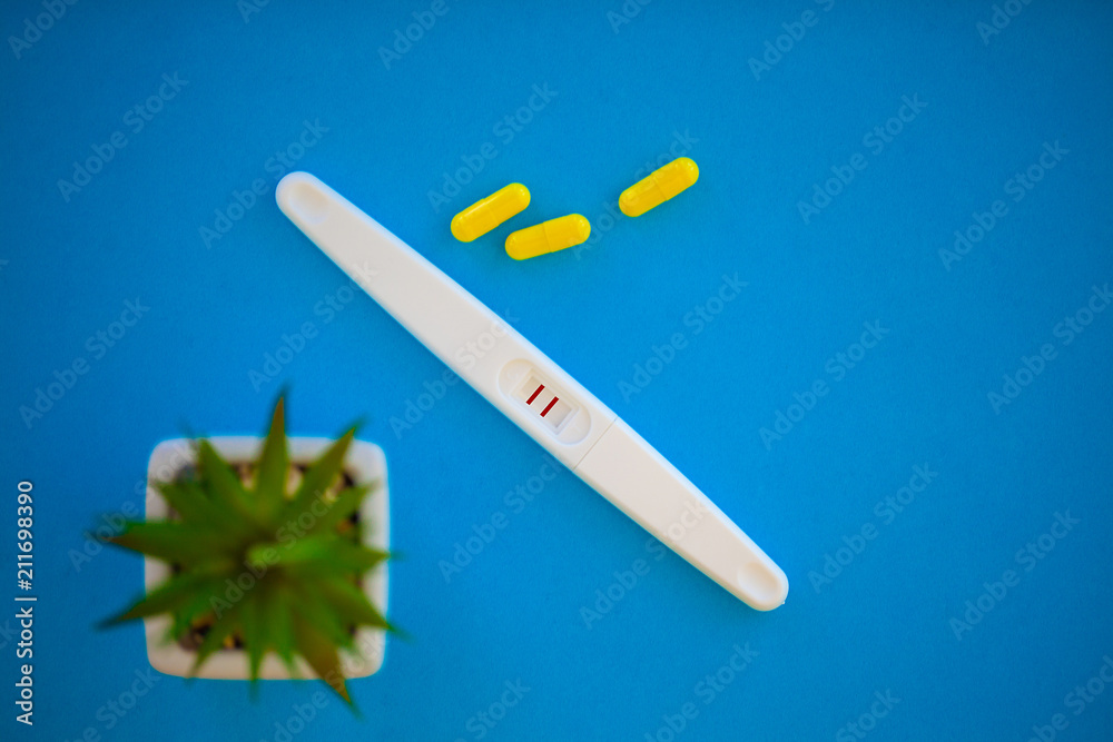 The result is positive. Close up of pregnancy test and contraceptive pills birth control concept on blue background The result is positive. Close up of pregnancy test and contraceptive pills birth control concept on blue background